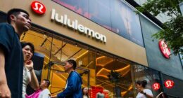 Pedestrians walk past a Lululemon retail store with its brand signage and interior displays visible through large glass windows.