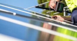 Unidentified electrician performing installation of solar panel on house roof using cordless screwdriver