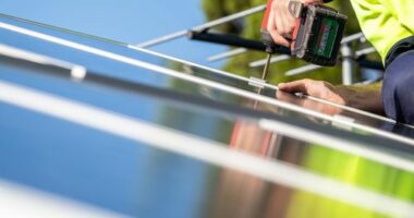 Unidentified electrician performing installation of solar panel on house roof using cordless screwdriver