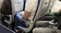 Passengers seated inside an airplane cabin with visible seat belts, legroom, and personal belongings during a commercial flight