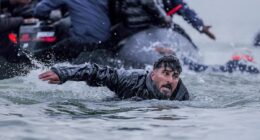 French police watch on as migrants wade into the sea to board boats