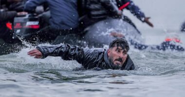 French police watch on as migrants wade into the sea to board boats