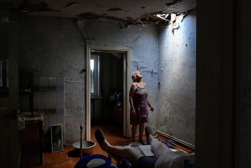 Zoya Shaposhnik 67 (left) looks up at the hole in her ceiling which was damaged this morning at approximately 9am in a missle strike where her ill husband (left) was sitting in their home in Krasnohorivka. Their roof and other parts of their home has been destroyed and Zoya has spent the day removing debris. Krasnohorivka, Ukraine. 16th June, 2022.