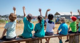 Students holding their hands up to volunteer or ask questions of their teacher at an outdoor nature class.