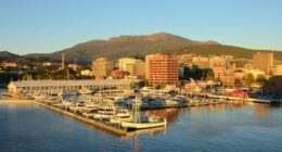 A view of Sullivans Harbor in Hobart, Tasmania on a clear day with Mt. Wellington rising in the background. The Broadcast Australia Tower, or NTA, sticks up on Mt. Wellington like a rocket poised for takeoff,